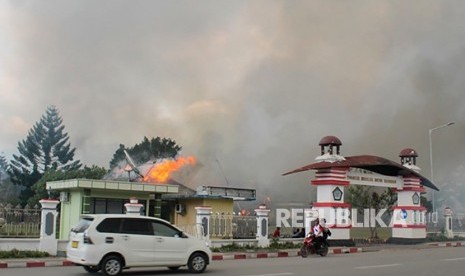 Pengendara melintasi Kantor Bupati Jayawijaya yang terbakar saat aksi unjuk rasa di Wamena, Jayawijaya, Papua, Senin (23/9/2019). 