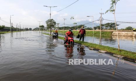 Pengendara mendorong sepeda motor menerobos banjir yang menggenangi jalan raya Porong, Sidoarjo, Jawa Timur, Selasa (16/2/2021). Curah hujan yang tinggi sejak Senin (15/2) malam mengakibatkan banjir yang merendam jalan raya Porong sehingga mengganggu kelancaran transportasi umum. 