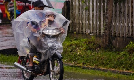 Pengendara motor menggunakan mantel saat melintas di tengah hujan turun di Kota Pekanbaru, Riau, Kamis (14/2/2019).