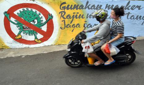 Pengendara motor menggunakan masker melintas di samping mural bergambar protokol kesehatan COVID-19 di jalan Roda 2 Gang Mesin RT 01/01, Kelurahan Babakan Pasar, Kota Bogor, Jawa Barat. Bogor kembali meperpanjang Pembatasan Sosial Berskala Mikro dan Komunitas (PSBMK) 