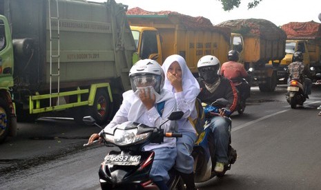 Pengendara motor menutup hidungnya saat melintasi sejumlah truk sampah milik Dinas Kebersihan dan Pertamanan Kota Bogor yang diparkir di pinggir jalan raya Paledang, Kota Bogor, Jawa Barat, Senin (4/1).