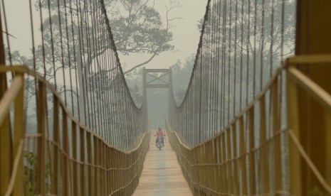 Pengendara roda dua menyeberangi jembatan yang diselimuti kabut asap di Desa Aur Gading, Batin XXIV, Batanghari, Jambi, Minggu (25/10). 