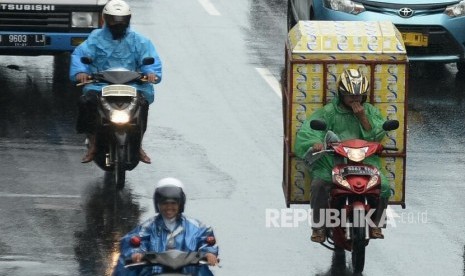 Pengendara sepeda motor menerobos hujan dengan menggunakan jas hujan.