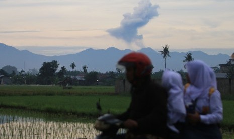 Pengendara sepeda motor melintas dengan latar belakang Gunung Sinabung menyemburkan material vulkanik tampak dari kawasan Sunggal (70 km dari Sinabung), Deli Serdang, Sumatera Utara, Selasa, (19/7). 