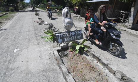 Pengendara sepeda motor melintas di dekat makam yang dibuat warga, di Labuan Panimba, Kabupaten Donggala, Sulawesi Tengah, Rabu (25/5/2022). Warga setempat memasang batu, kayu, dan tanaman di jalan tersebut sebagai bentuk protes dan kekecewaan mereka karena jalan rusak dan bertdebu yang tidak kunjung diperbaiki.