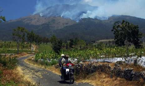 Pengendara sepeda motor melintas di perladangan berlatar belakang kebakaran hutan gunung Sumbing Desa Pagergunung, Bulu, Temanggung, Jawa Tengah, Selasa (11/9). 