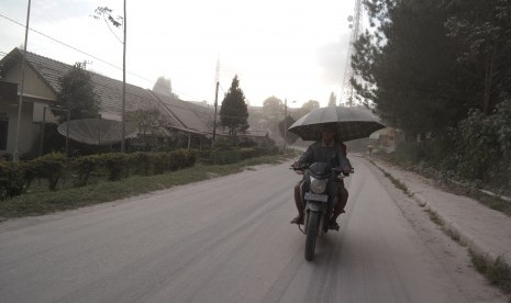 Pengendara sepeda motor melintas saat hujan abu vulkanik erupsi Gunung Sinabung, di Brastagi, Karo, Sumatera Utara, Jumat (26/6).