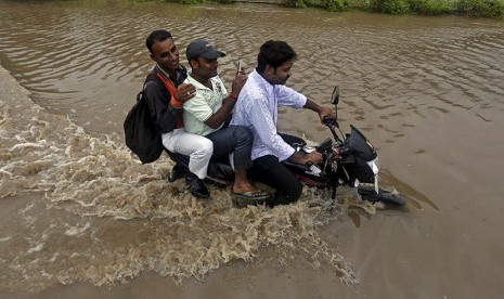  Pengendara sepeda motor melintasi jalan yang terendam air banjir, usai hujan deras di Ahmedabad, India, Selasa (28/7).