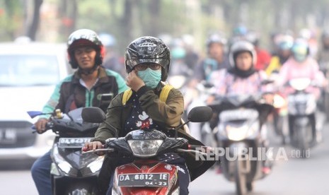 Pengendara sepeda motor menggunakan masker pelindung pernapasan saat melintas di jalan Brig Jend Hasan Basri yang diselimuti kabut asap di Banjarmasin, Kalimantan Selatan, Senin (14/10/2019).