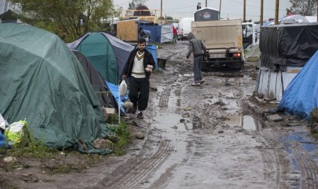 Pengungsi asal Irak, Jamal, membawa makanan melewati kamp pengungsian yang basah tanahnya akibatnya cuaca dingin di penghujung tahun di Calais, bagian utara Prancis, akhir bulan Oktober 2015.