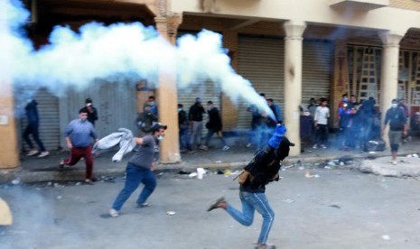 Pengunjuk rasa antipemerintah berlari  melemparkan tabung gas air mata ke arah pasukan polisi anti huru hara selama bentrokan dengan pasukan polisi anti huru hara di jalan Al Rasheed  Baghdad, Irak, Senin (25/11/2019).