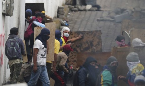 Pengunjuk rasa antipemerintah berlindung di balik perisai kayu saat bentrok dengan polisi di dekat Dewan Nasional saat penerapan jam malam di Quito, Ekuador, Ahad (13/10).