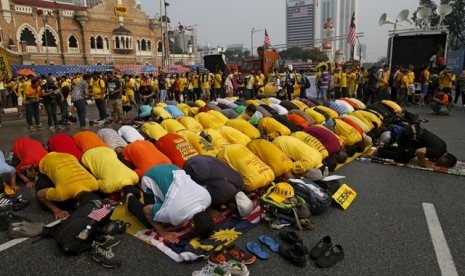 Pengunjuk rasa berkaus kuning menjalankan shalat di Dataran Merdeka, Ahad (30/8). Mereka berunjuk rasa menuntut pengunduran diri PM Malaysia, Najib Razak, yang terlilit dugaan korupsi.