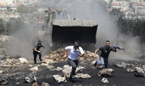 Pengunjuk rasa berlari di depan buldoser militer Israel saat bentrok dengan pasukan Israel saat aksi protes menentang pemukiman Yahudi di Qadomem, Kofr Qadom dekat Nablus, Tepi Barat, Palestina, Jumat (27/6).