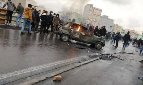 Pengunjuk rasa Iran berdiri di sekitar kendaraan dibakar selama bentrokan menyusul kenaikan harga bahan bakar di Teheran, Iran.