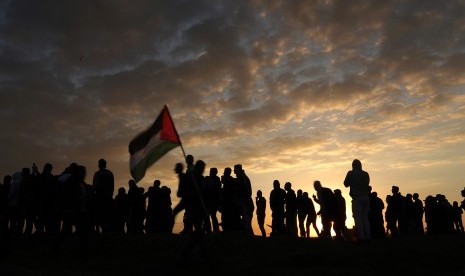 Pengunjuk rasa melambaikan bendera Palestina saat terjadi bentrokan di dekat perbatasan dengan Israel di timur Kota Gaza, Jumat (15/12). Demonstran memprotes keputusan Presiden AS Donald Trump mengakui Yerusalem sebagai Ibu Kota Israel. 