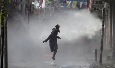 Pengunjuk rasa mengenakan masker melarikan diri saat polisi menembakkan gas air mata di peringatan Hari Buruh di kawasan Okmeydani, Istanbul, Turki.