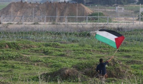 Pengunjuk rasa mengibarkan bendera Palestina di depan tentara Israel setelah terjadi bentrokan di dekat perbatasan Israel dan Jalur Gaza, (20/11).