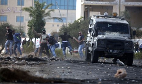 Pengunjuk rasa Palestina melemparkan batu ke kendaraan militer Israel selama bentrokan dengan pasukan Israel di dekat Ramallah, Tepi Barat, Kamis, 8 Oktober 2015. 