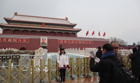 Pengunjung berpose di depan gerbang utama objek wisata Kota Terlarang, Beijing, beberapa saat setelah hujan salju, Kamis (14/2/2019) petang.