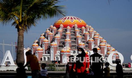 Pengunjung melintas di Pantai Losari dengan latar belakang Masjid 99 Kubah di Makassar, Sulawesi Selatan, Sabtu (22/5/2021). Pembangunan masjid yang diharapkan menjadi ikon baru Kota Makassar tersebut telah memasuki tahap tiga yang ditargetkan rampung pada 2022 dengan anggaran yang masih dibutuhkan sebesar Rp72 miliar. 