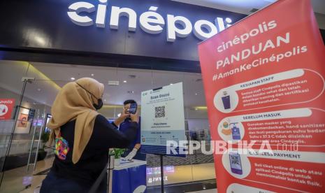 Pengunjung memindai kode batang (QR Code) melalui aplikasi PeduliLindungi sebelum memasuki bioskop Cinepolis. ilustrasi 