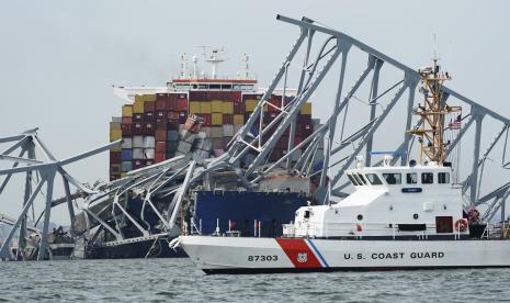 Penjaga Pantai melewati kapal kargo yang terjebak di bawah bagian struktur Jembatan Francis Scott Key setelah kapal tersebut menabrak jembatan, di Baltimore.