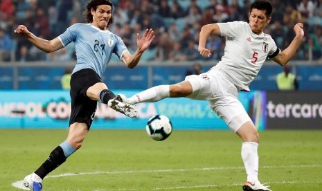 Penyerang Uruguay Edinson Cavani (kiri) dijaga bek Jepang Naomichi Ueda.