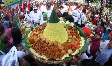 People struggle to seize a cone-shaped rice or locally called Nasi Tumpeng in a tumpeng festival Solo (illustration)  