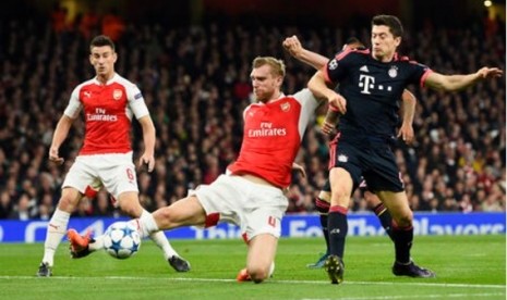 Per Mertesacker (tengah) berusaha menghalau bola dari kejaran Robert Lewandowski