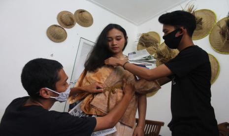 Perajin memakaikan busana batik etnik hasil karyanya kepada seorang model sebelum dilakukan pemotretan di rumah produksi Batik Hamparan Rintik,Malang, Jawa Timur.