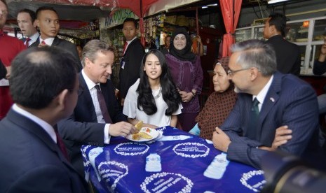 Perdana Menteri Inggris David Cameron (kedua kiri) didampingi Dubes Inggris untuk Indonesia Moazzam Malik (kanan) dan artis Maudy Ayunda (tengah) menikmati pisang goreng di warung halaman Masjid Agung Sunda Kelapa, Jakarta, Selasa (28/7).