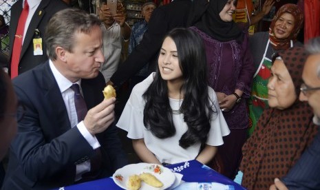 Perdana Menteri Inggris David Cameron (kiri) didampingi Dubes Inggris untuk Indonesia Moazzam Malik (kanan) dan artis Maudy Ayunda (kedua kiri) menikmati pisang goreng di warung halaman Masjid Agung Sunda Kelapa, Jakarta, Selasa (28/7).