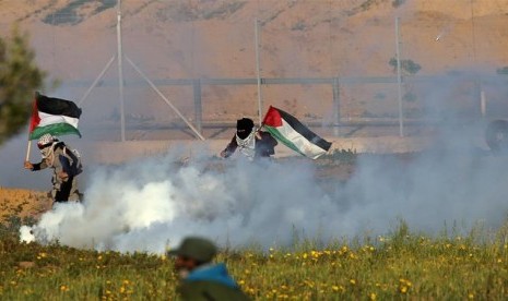 Perempuan Palestina berlari membawa bendera Palestina untuk menghindari serangan gas air mata yang dilancarkan tentara Israel.