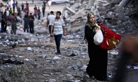 Perempuan Palestina membawa barang di tengah reruntuhan gedung di Jalur Gaza.