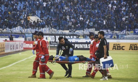 Persib Bandung Imbang Melawan Madura United. Penyerang Persib Bandung Ezechiel Ndouasel ditandu keluar lapangan pada pertandingan Sepak Bola Liga 1 2019 di Stadion Si Jalak Harupat, Kabupaten Bandung, Ahad (23/6). 