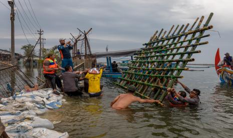 Personel kepolisian dari Polsek Kesatuan Pelaksanaan Pengamanan Pelabuhan (KP3) Tanjung Emas Semarang bersama warga dan relawan bergotong royong menutup tembok kawasan industri atau tanggul yang jebol dengan konstruksi pagar bambu dan karung berisi pasir dan batu di kawasan industri Pelabuhan Tanjung Emas Semarang, Jawa Tengah, Rabu (25/5/2022). PT Pelindo (Persero) Regional 3 Tanjung Emas Semarang menyiapkan 3.600 karung berisi pasir dan batu serta pagar bambu untuk membuat tanggul darurat guna menutup tanggul yang jebol.