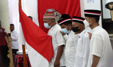 Perwakilan dari jaringan anggota Negara Islam Indonesia (NII) memegang bendera Merah Putih ketika pembacaan sumpah saat acara cabut baiat massal mantan anggota Negara Islam Indonesia di Kabupaten Dharmasraya, Sumatera Barat, Rabu (27/4/2022). Sebanyak 391 orang pengikut NII melakukan sumpah setia kepada Negara Kesatuan Republik Indonesia (NKRI).