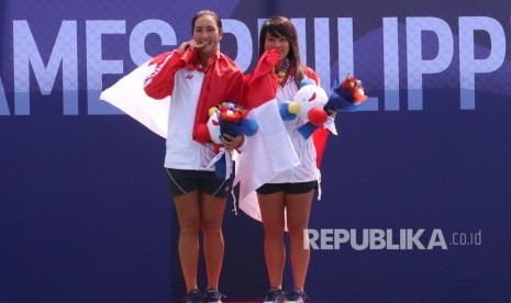 Petenis tunggal putri Indonesia Aldila Sutjiadi (kiri) menggigit medali emas bersama rekannya Priska Madelyn yang meraih medali perunggu seusai mengikuti upacara penganugerahan medali tenis tunggal putri SEA Games 2019 di lapangan Rizal Memorial Tennis Centre, Manila, Filipina, Jumat (6/12/2019).