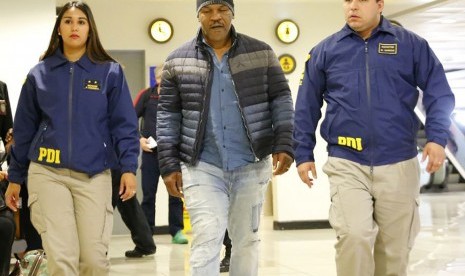 Petinju Mike Tyson diapit petugas Kepolisian Chile atau PDI, Kamis (10/11). Ia ditolak masuk Chile karena dianggap memiliki catatan kriminal di negaranya sendiri.