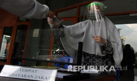 Petugas amil zakat dengan menggunakan pelindung wajah dan sarung tangan plastik melayani warga muslim yang membayar zakat fitrah di Masjid At Thoharoh, Ciputat, Tangerang Selatan, Banten. Kementerian Agama (Kemenag) dan Majelis Ulama (MUI) Kota Tangerang Selatan (Tangsel) mengimbau warga Tangsel melaksanakan salat Idul Fitri di rumah masing-masing. Imbauan yang dikeluarkan tersebut mengacu pada protokol kesehatan dalam pencegahan dan penularan virus Corona atau Covid-19.