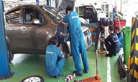 Petugas bengkel sedang memperbaiki mobil pelanggan