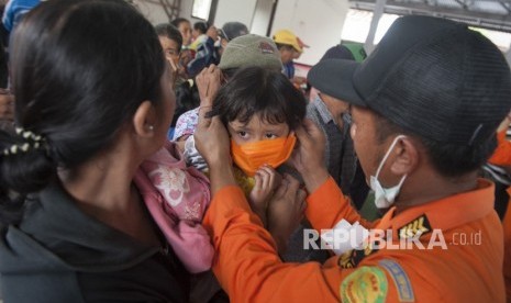 Petugas BPBD memasangkan masker kepada seorang anak pengungsi Gunung Agung di lokasi penampungan Desa Bebandem, Karangasem, Bali, Ahad (26/11).