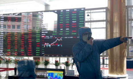 Petugas dengan pakaian pelindung bekerja di depan layar yang menunjukkan pergerakan saham di Shanghai Stock Exchange, Shanghai, China, Jumat (14/2). Saham-saham China menghapus kerugian awal menjadi ditutup lebih tinggi pada perdagangan Jumat (21/2).