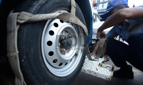 Petugas Dinas Perhubungan memasangkan tali di ban sebuah taksi saat melakukan penertiban parkir liar di kawasan Hasyim Ashari, Jakarta Pusat, Selasa (24/3).  (Republika/Raisan Al Farisi)