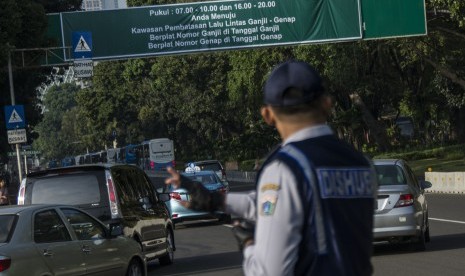 Petugas Dinas Perhubungan mengatur arus lalu lintas saat uji coba penerapan sistem lalu lintas pelat ganjil-genap di Jalan Medan Merdeka Barat, Jakarta, Rabu (27/7).