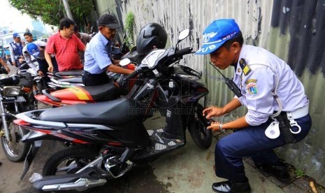   Petugas Dishub DKI mencabut pentil ban motor dan mobil yang parkir sembarangan di Jalan Matraman, Jakarta Timur, Senin (10/3).   (Republika/Yasin Habibi)