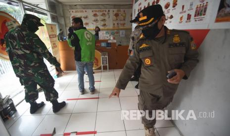 Petugas gabungan memberi himbauan untuk menjaga jarak antrean saat patroli penegakan aturan Pembatasan Sosial Berskala Besar (PSBB) di salah satu restoran di kawasan Kalibata, Jakarta, Jumat (17/4/2020). Patroli oleh petugas gabungan Polisi, TNI, dan Satpol PP tersebut dilakukan guna mencegah penyebaran COVID-19. 