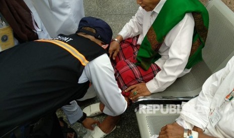 Petugas haji Indonesia memakaikan sandal pada jamaah yang kehilangan di Gerbang 21 Masjid Nabawi, Jumat (27/7). Tim kesehatan membagikan ribuan sandal mengingat berbahayanya berjalan-jalan tanpa sandal di tengah cuaca panas Madinah.