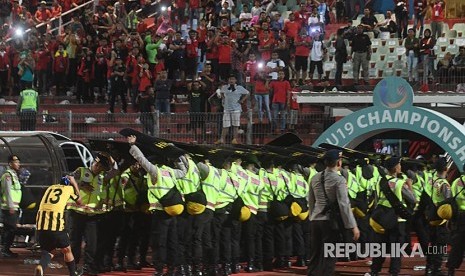 Petugas keamanan berusaha melindungi pesepak bola  Malaysia U19 Mohamad Izzuddin (kiri) dari lemparan suporter Indonesia usai laga semi final Piala AFF U19 di Gelora Delta Sidoarjo, Sidoarjo, Jawa Timur, Kamis (12/7). 